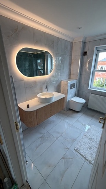 Newly fitted bathroom with wall-hung vanity, backlit mirror and marble-effect tiling