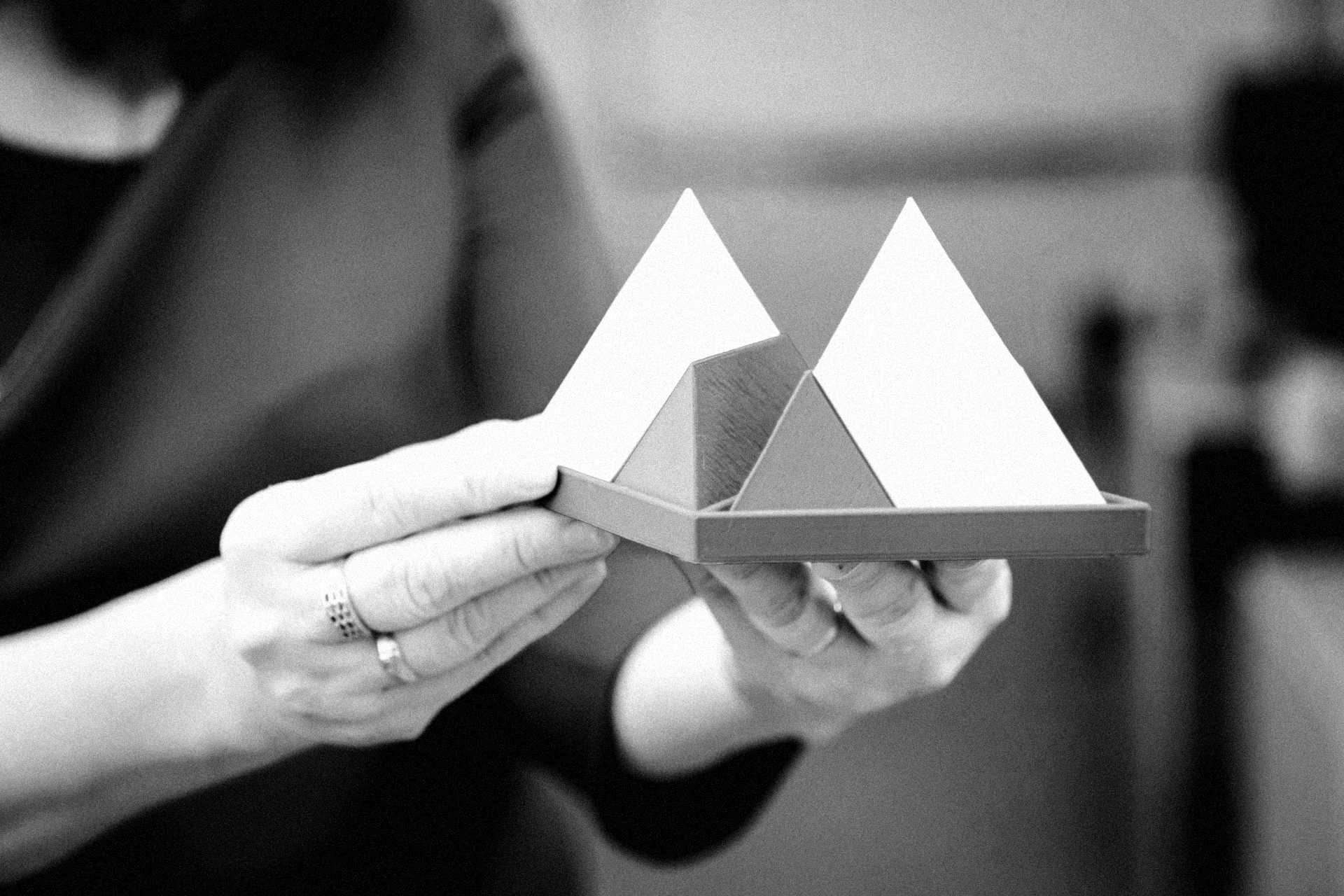 Person holding a small model of two pyramid shapes on a rectangular base.