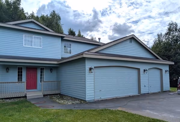 Two-story blue house with a red front door, three-car garage, and green lawn under cloudy sky.