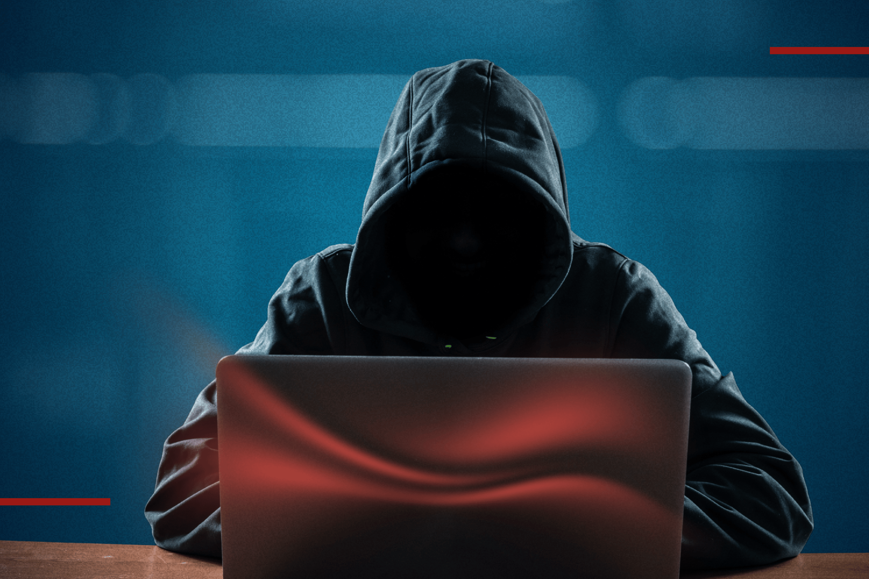 Person mit Hoodie sitzt vor einem Laptop, Gesicht durch die Kapuze verdeckt, im Hintergrund blaues Licht mit roten Akzentlinien – Symbolbild für Cyberkriminalität und IT-Sicherheit.