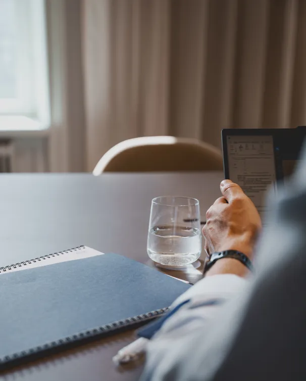 Person holding an e-reader or tablet at a table with a glass of water and notebooks.