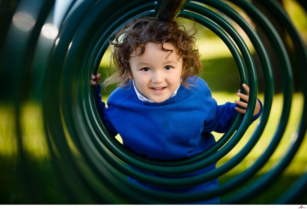 Small boy in a blue sweater peeking through a green spiral climber at a Halifax playground