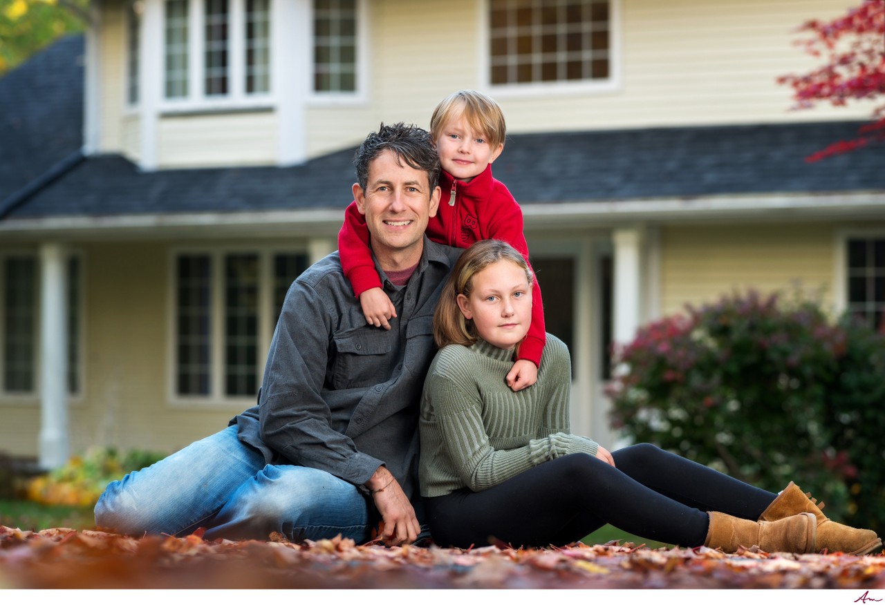 Dad sitting in fall leaves with his two kids in front of their home, on location in Halifax