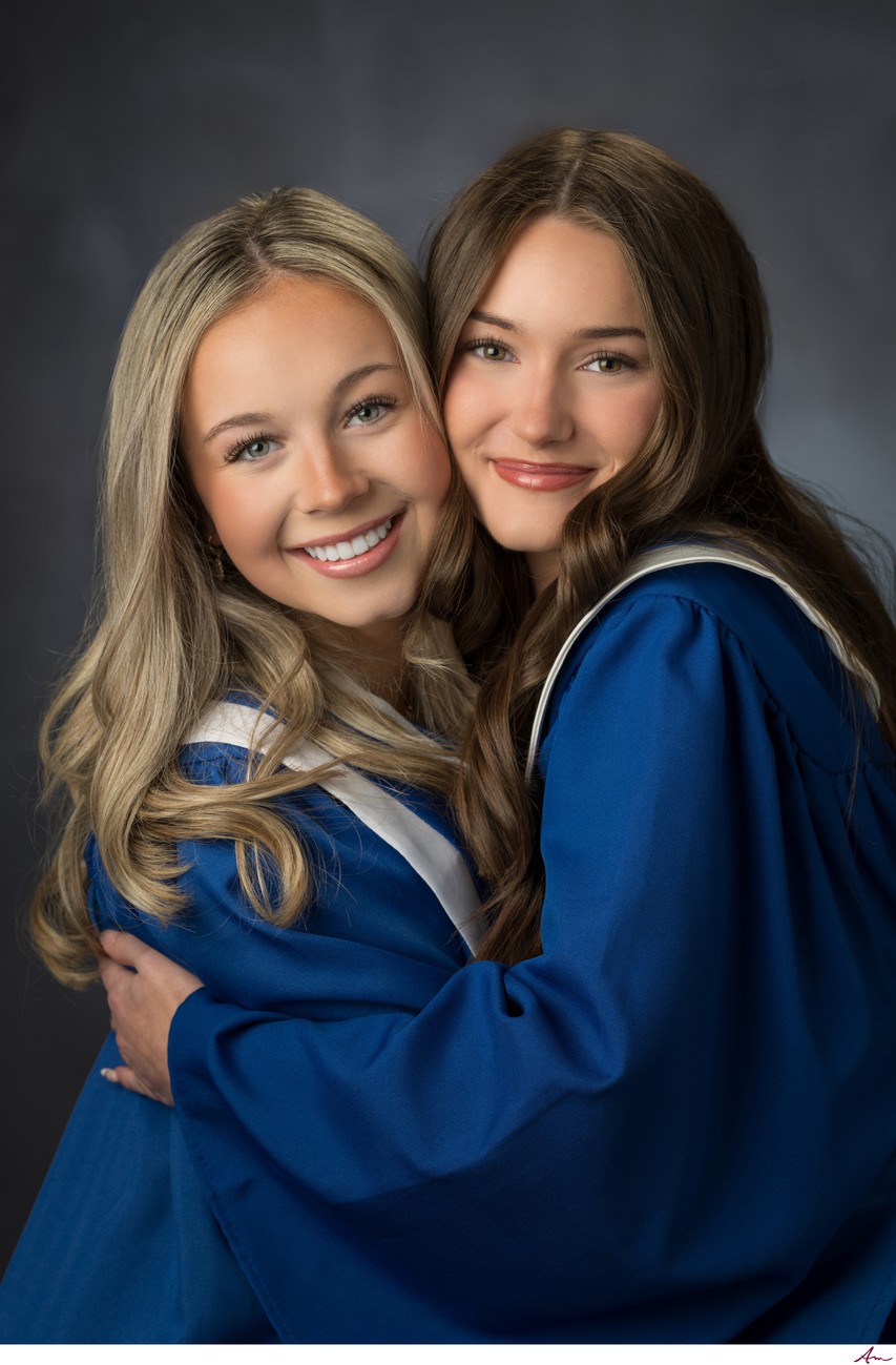 Two Charles P. Allen graduates in blue gowns hugging and laughing, best friends grad portrait
