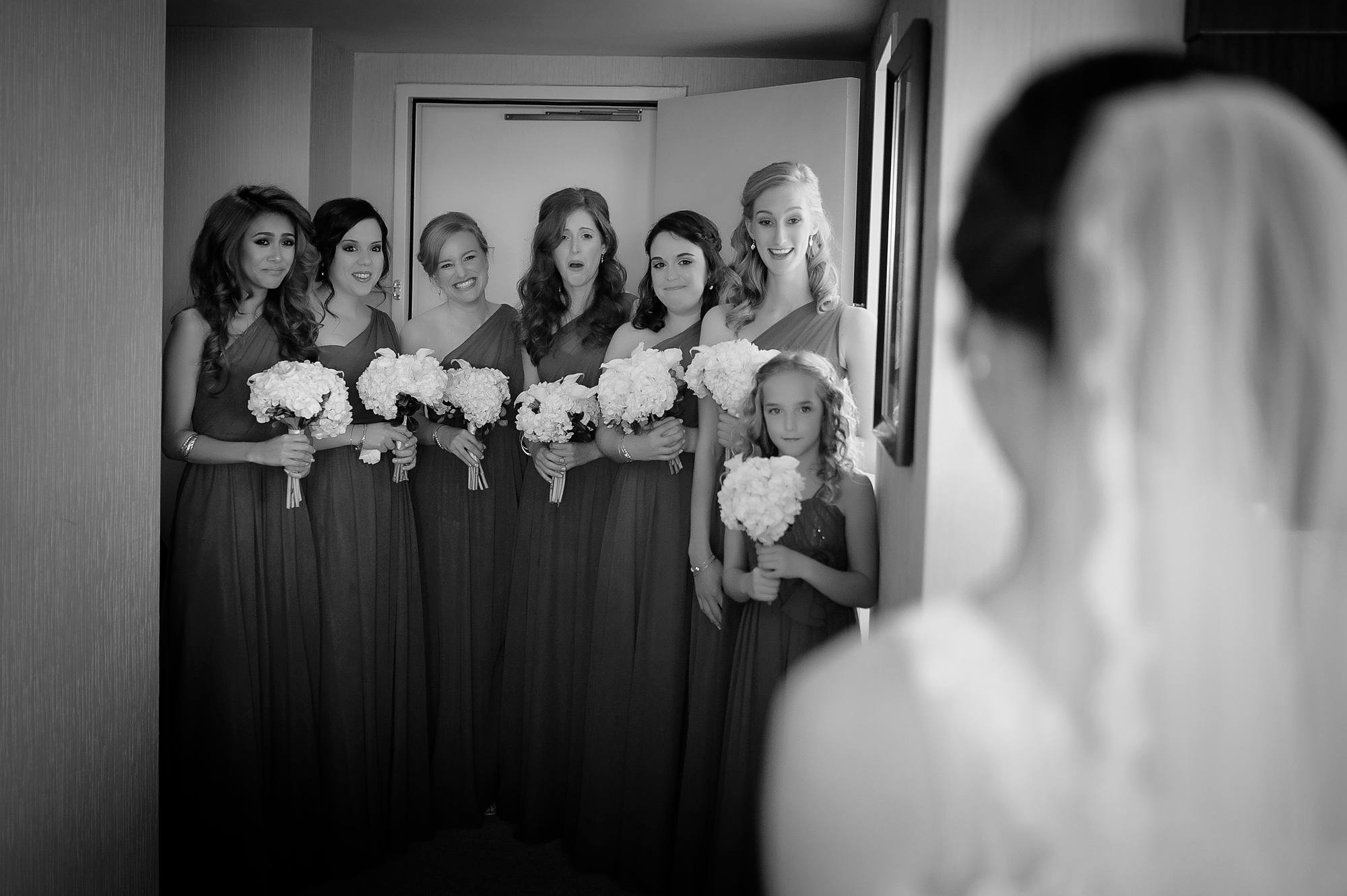 Bridesmaids reacting as they see the bride in her dress for the first time, black and white