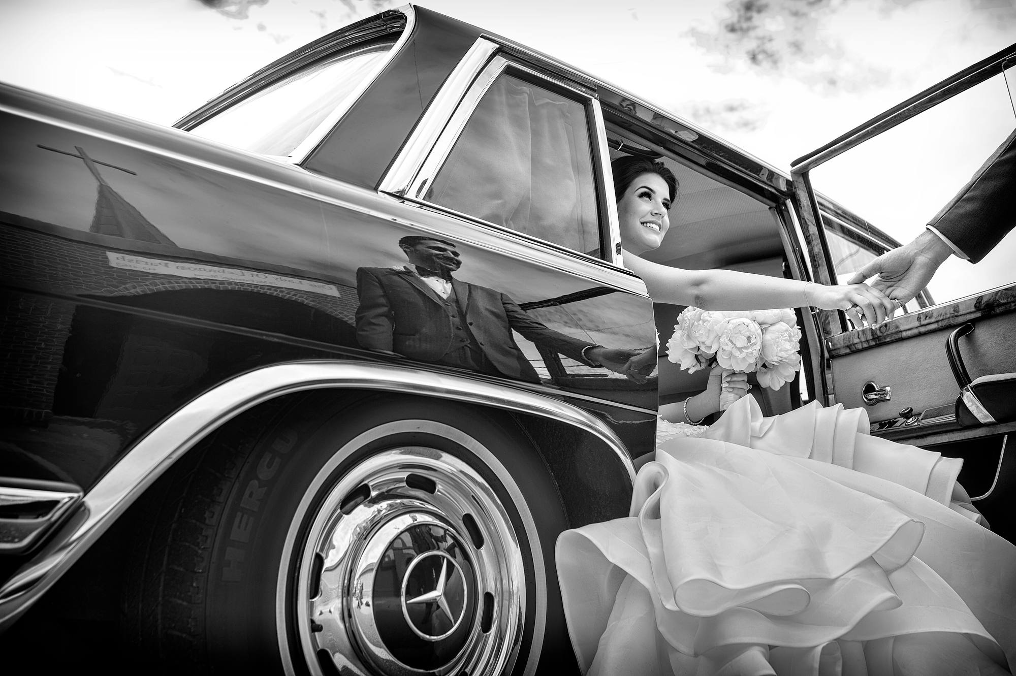 Groom helping his bride out of a vintage Mercedes, church steeple reflected in the fender, Halifax