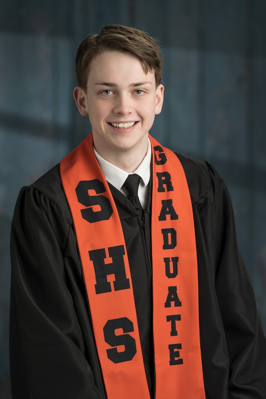 Sackville High graduate in black gown and orange SHS stole at a barn door, Hammonds Plains