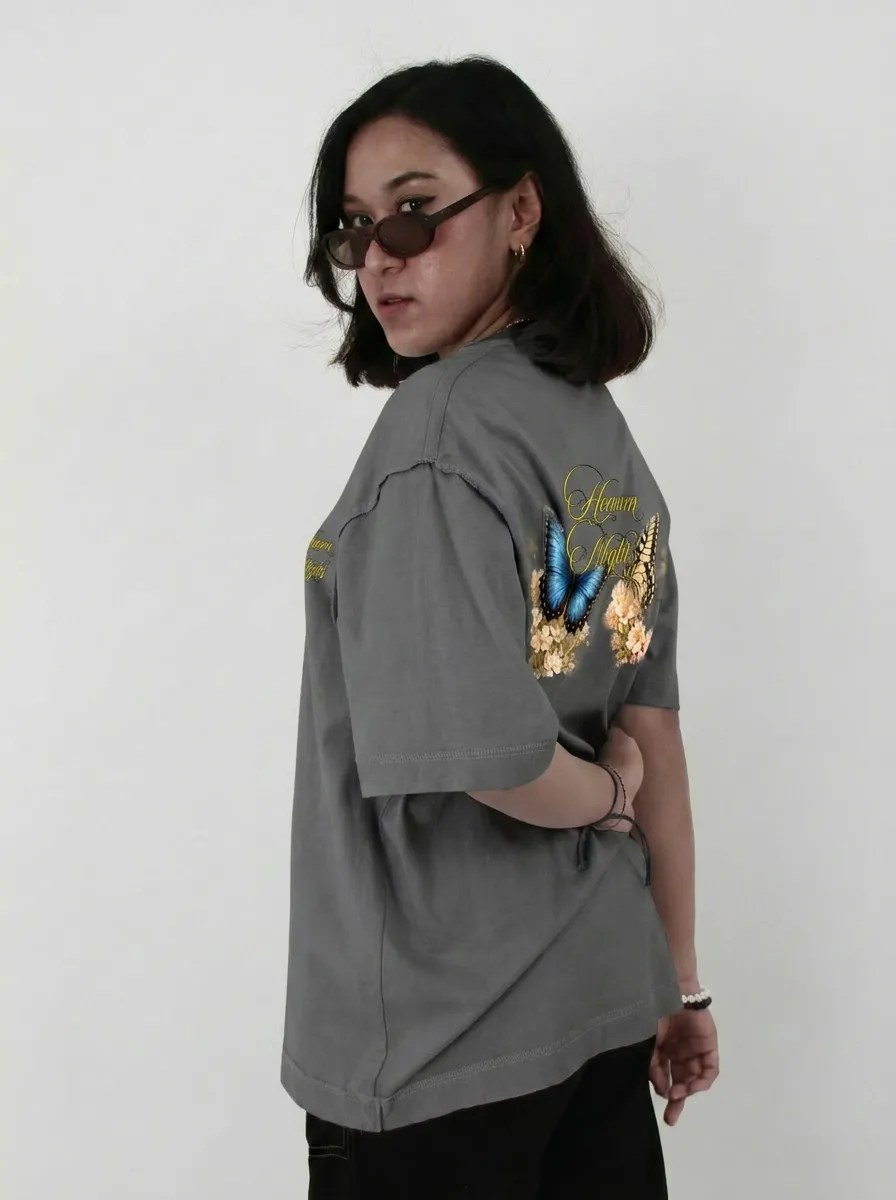 Woman wearing HVN NHTZ 'Denim Nights' gray shirt with butterfly and floral print on back, looking over her sunglasses.