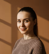 Smiling woman with dark hair wearing a brown sweater against a warm, shadowed background.