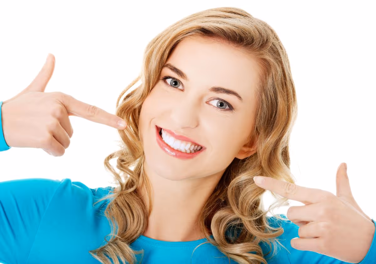 Smiling woman with blonde curly hair pointing at her white teeth showing bright smile.