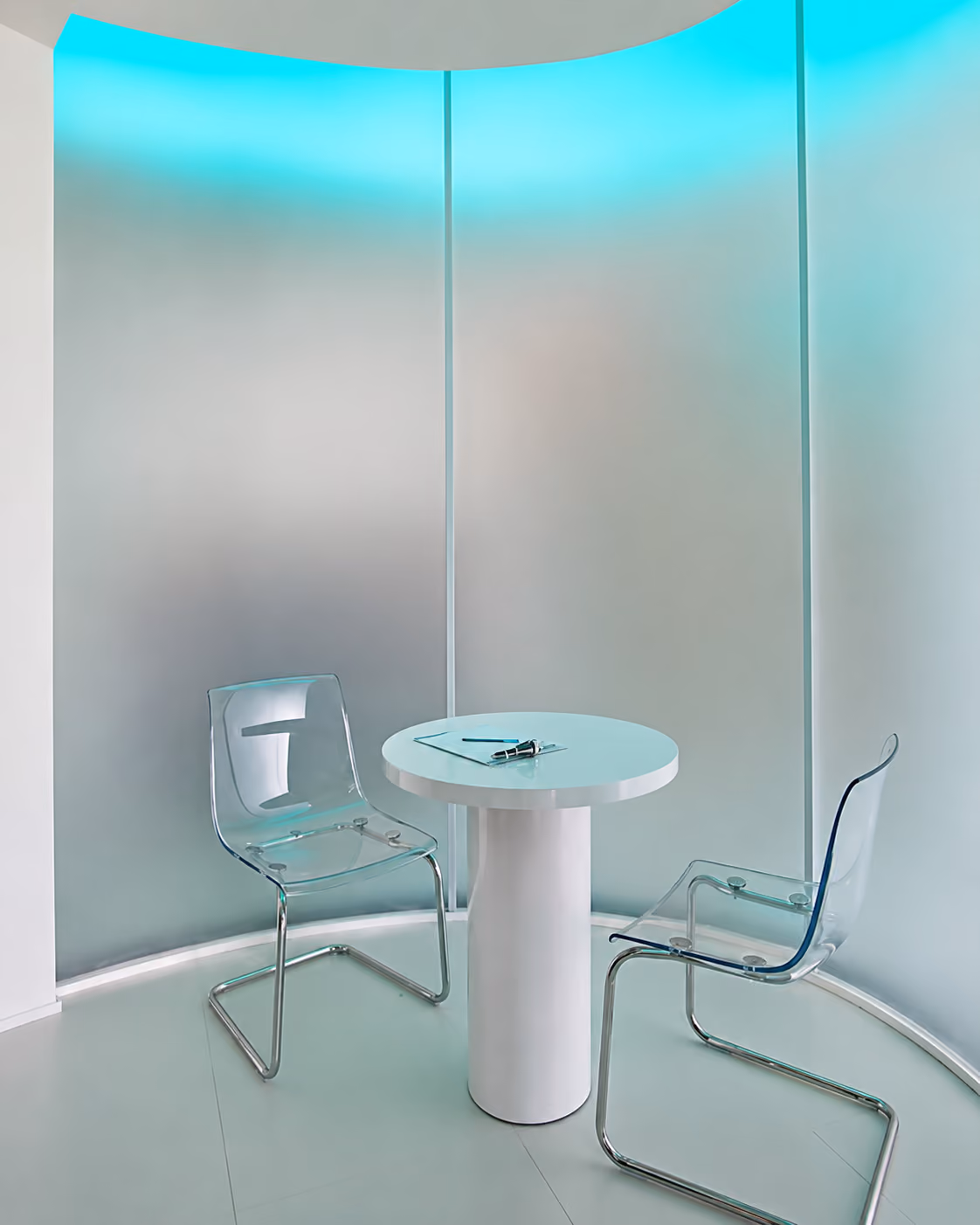Modern small white round table with two transparent chairs in a curved room with blue LED lighting.