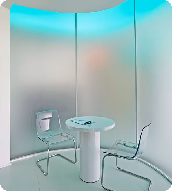 Modern small white round table with two transparent chairs in a curved room with blue LED lighting.