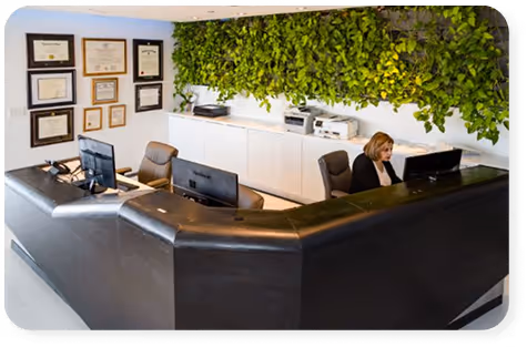 Office reception area with a woman working at a computer behind a black desk and a green wall behind her.
