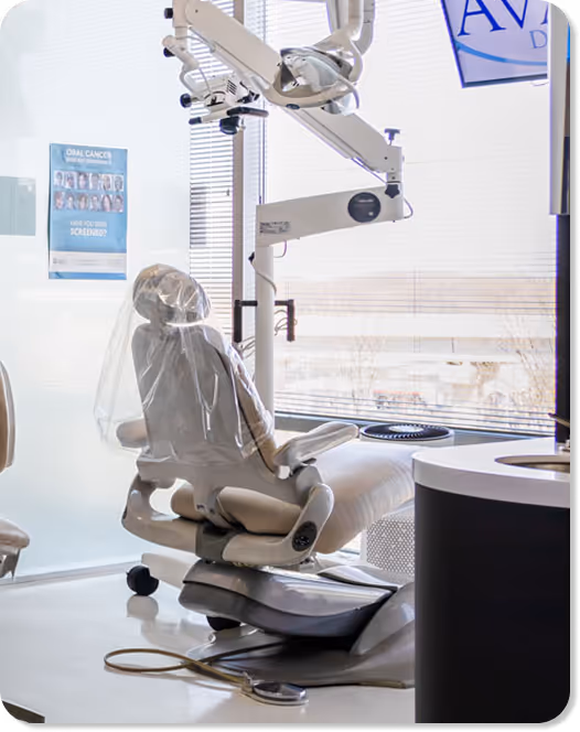 Modern dental chair with protective plastic cover and overhead dental equipment near window blinds.