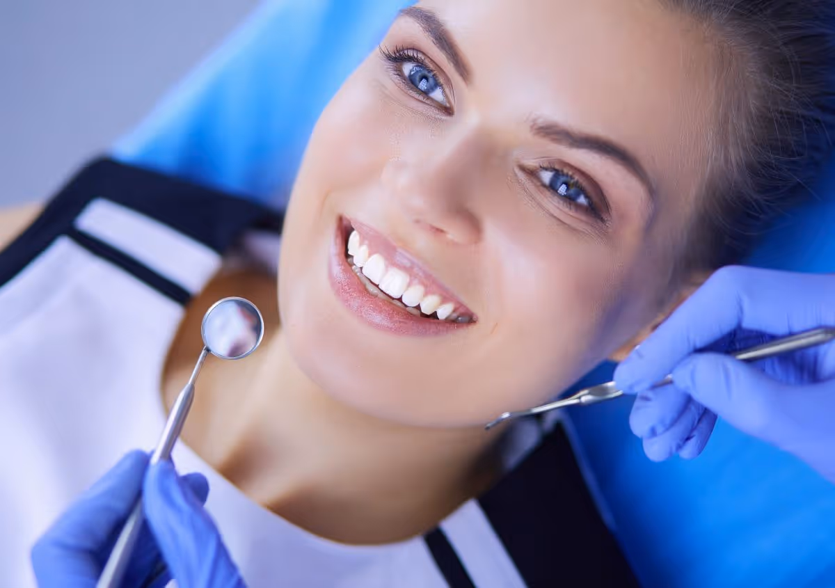 Woman smiling while a dentist with gloves examines her teeth with dental tools.