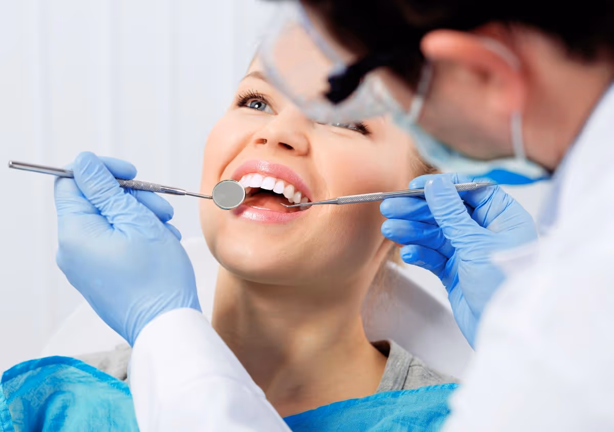 Dentist in gloves examining a smiling woman's teeth with dental mirror and probe.