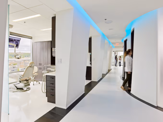 Modern dental clinic hallway with patient rooms and a blue light strip on the ceiling.