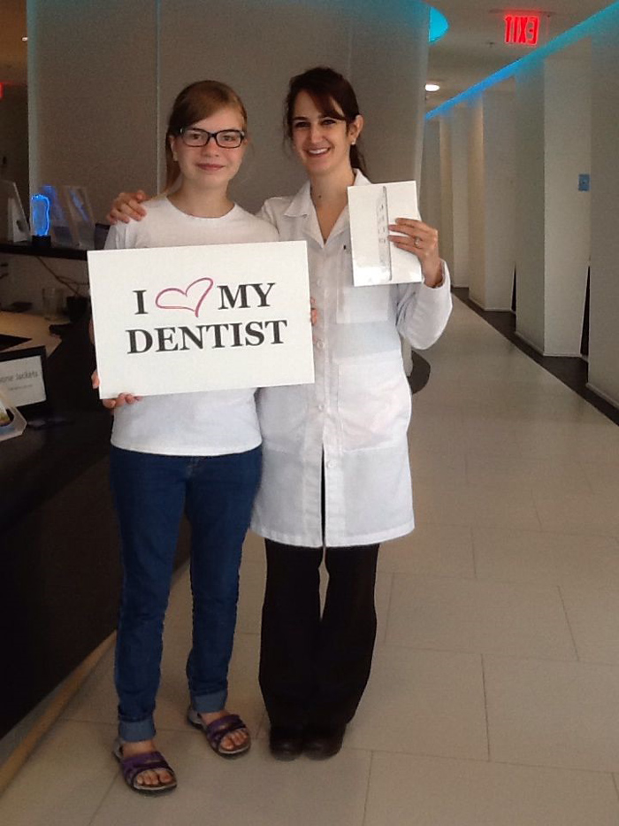 Smiling dentist and patient holding sign that says 'I love my dentist' in dental office.