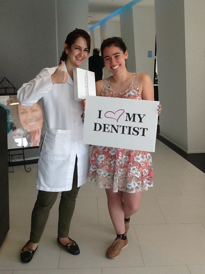 Smiling dentist and patient holding a sign that says 'I heart my dentist' inside a clinic.