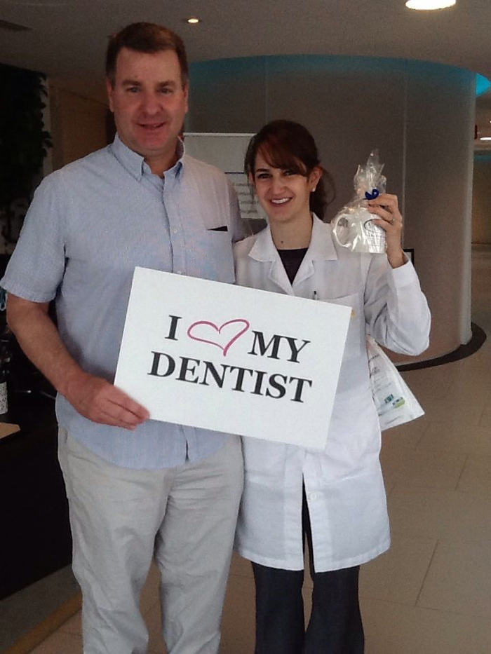 Man and woman in a white coat hold a sign saying I love my dentist in a dental office.