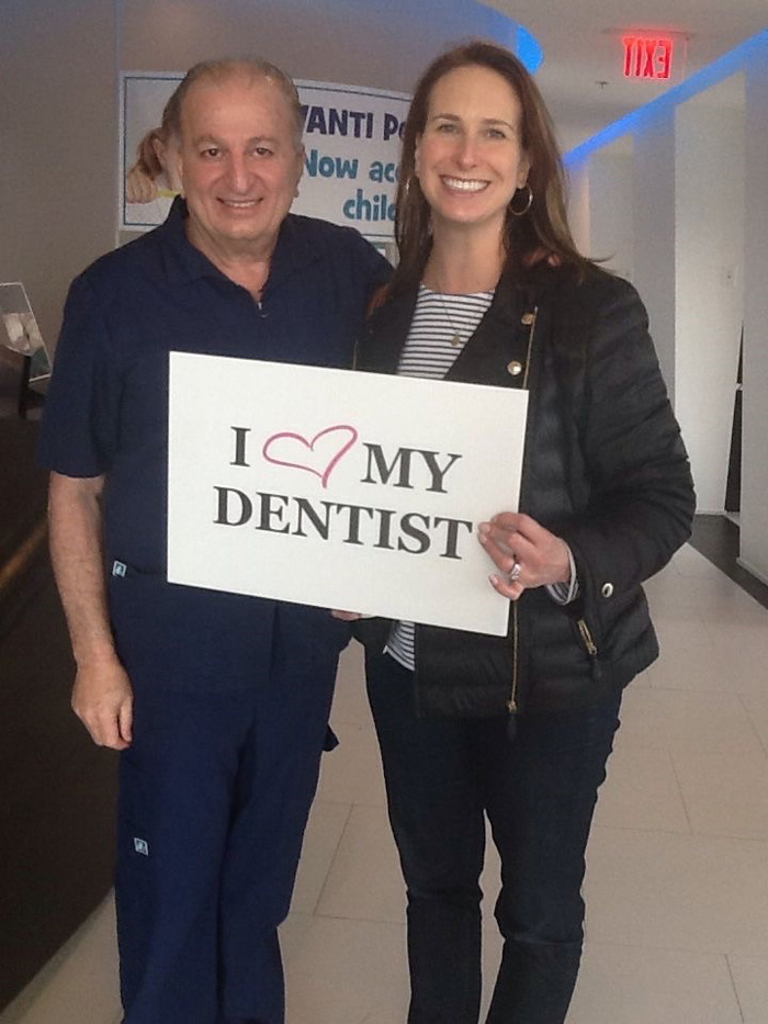 Smiling man and woman holding a sign that says 'I love my dentist' inside a dental office.