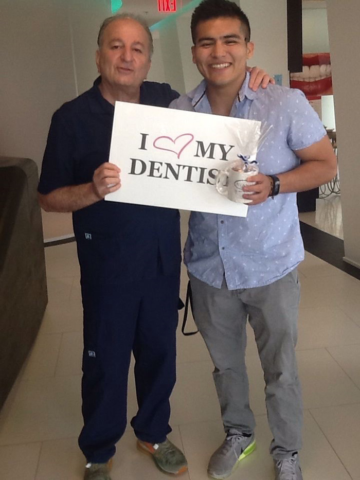 Two men smiling, one holding a sign that says I love my dentist with a heart symbol.