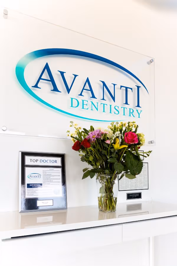 Reception desk with Top Doctor award, flower bouquet, and Avanti Dentistry logo on wall behind.