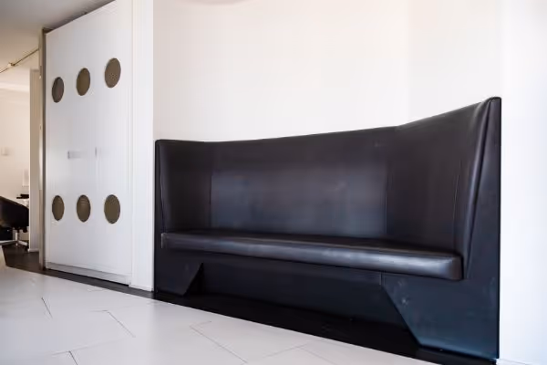 Modern black leather bench in a white, minimalist room with sliding white doors featuring circular cutouts.