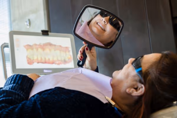 Patient wearing sunglasses looking at her teeth in a hand mirror in a dental clinic.