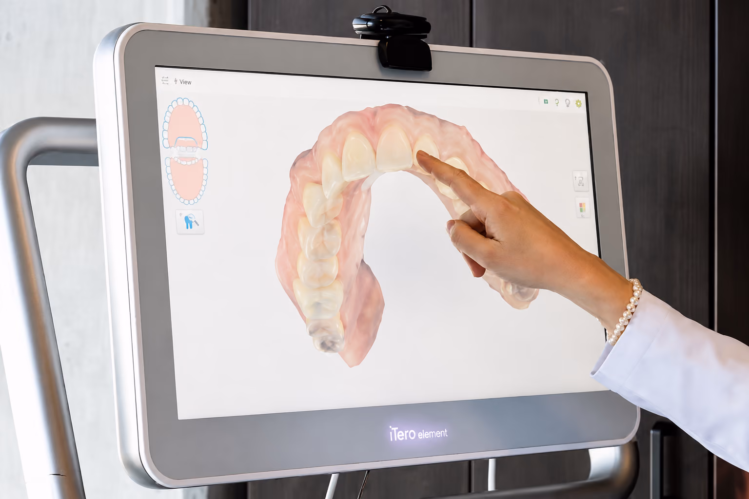 Hand pointing to a digital dental 3D model of teeth displayed on a screen.