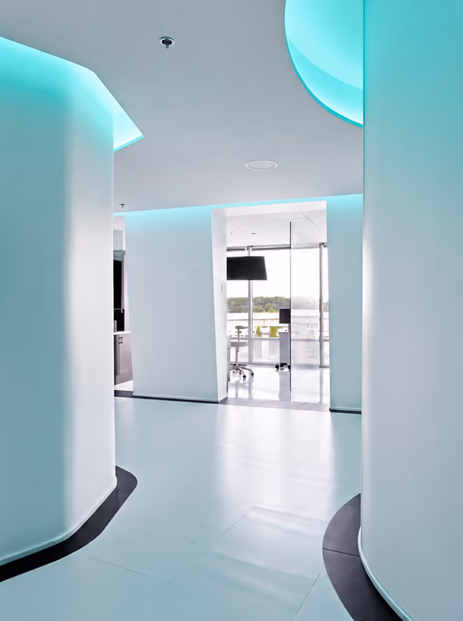 Modern interior hallway with curved white walls and turquoise LED ceiling lighting.