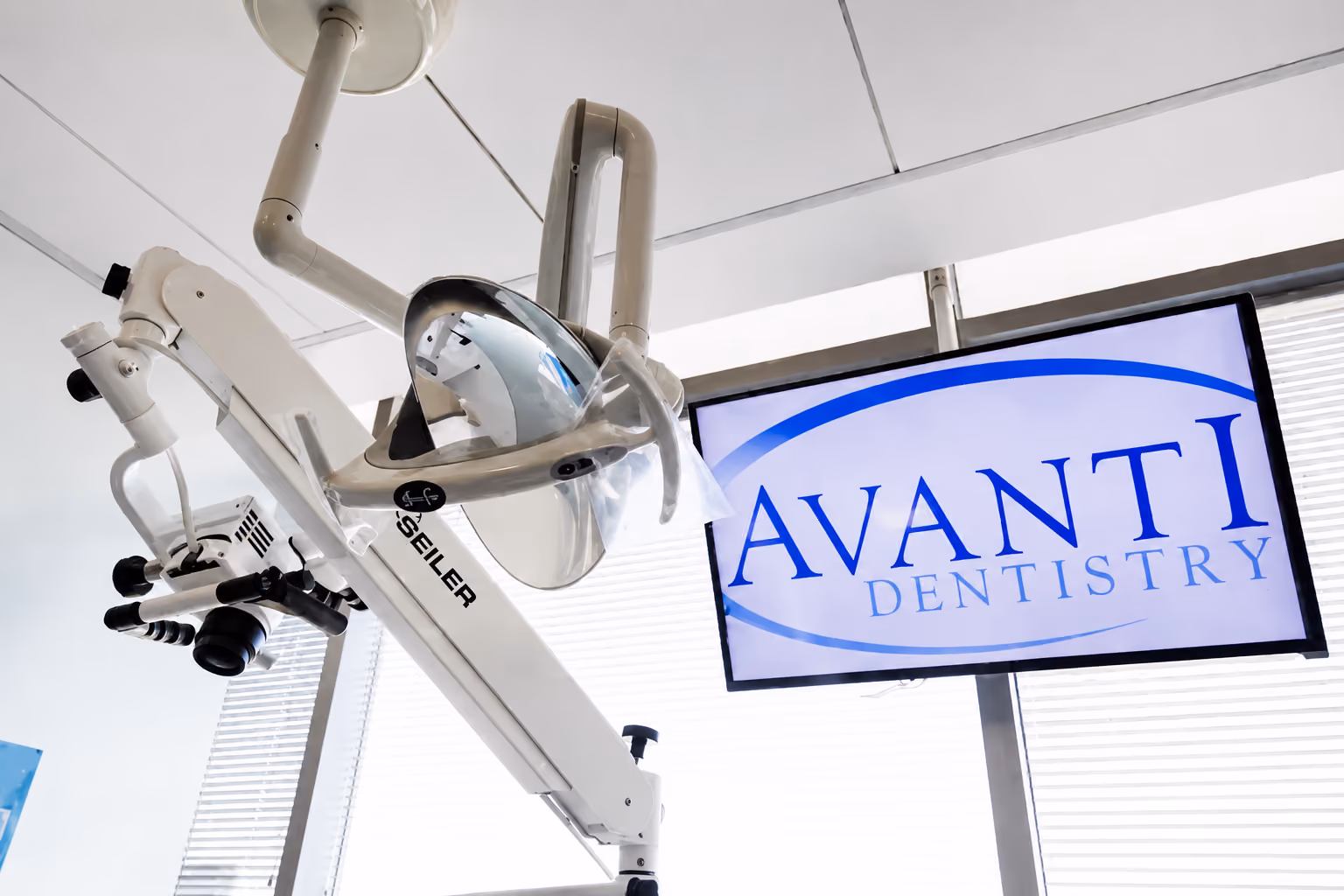 Dental clinic equipment including a light and a screen showing Avanti Dentistry logo.