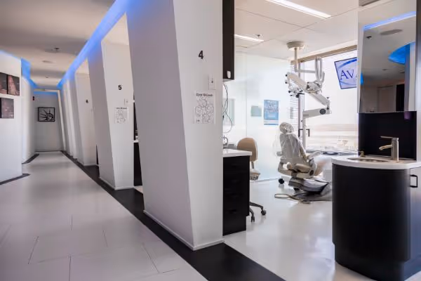 Modern dental clinic hallway with numbered treatment rooms and dental chair visible through open door.