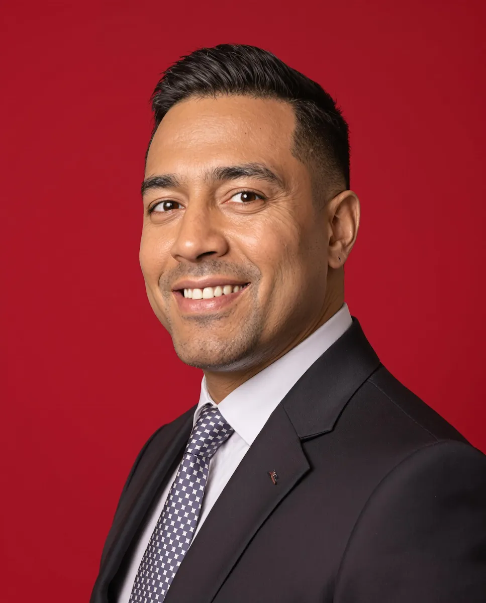 Smiling man in black suit and patterned tie against a red background.