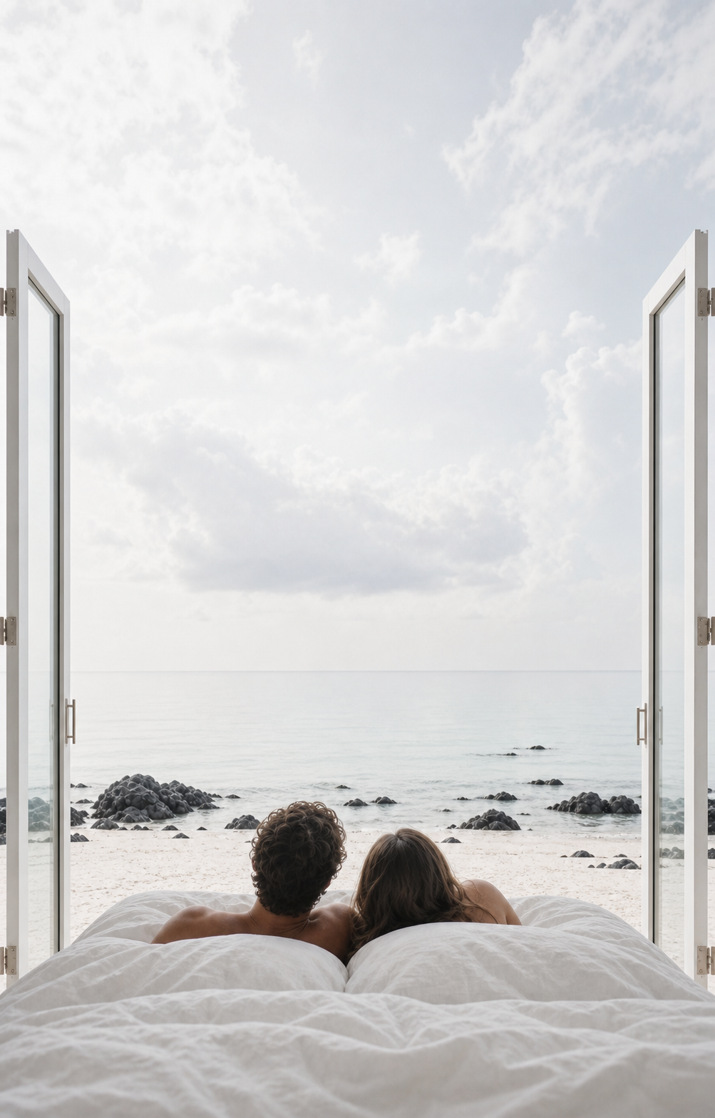 Couple relaxing in bed while looking through open doors toward the ocean
