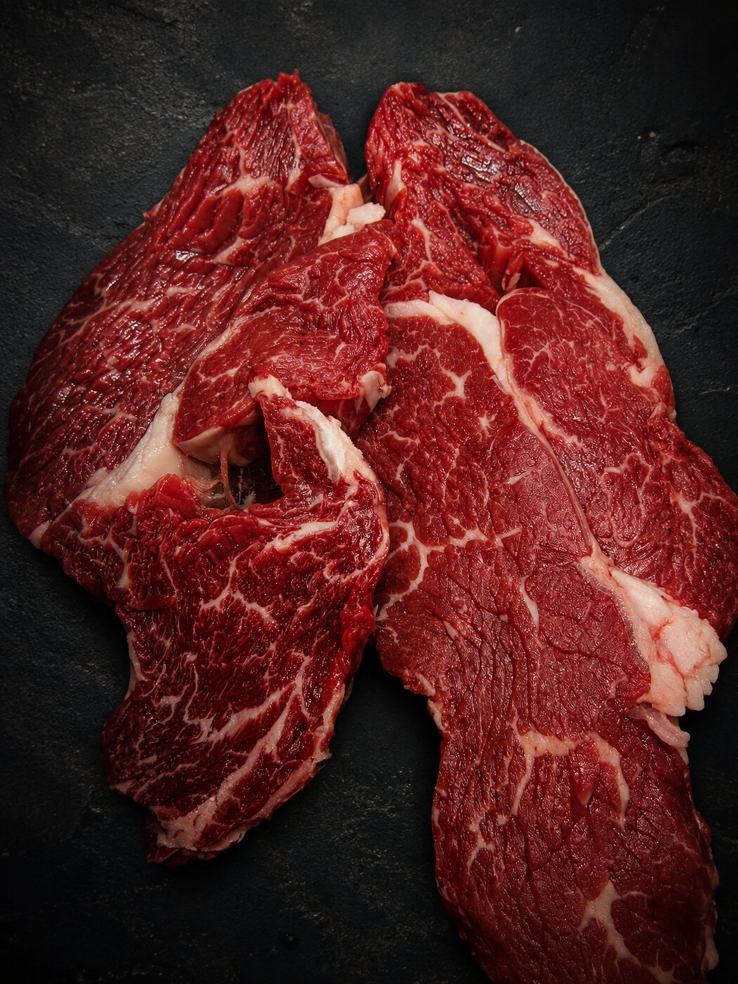 Marbled ribeye cuts on dark slate at Deenihan's Prime Cuts.