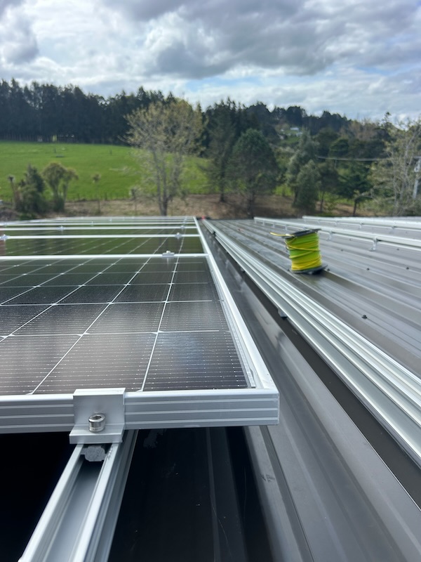 Close-up of solar panel frames installed on a rooftop with green countryside in the background