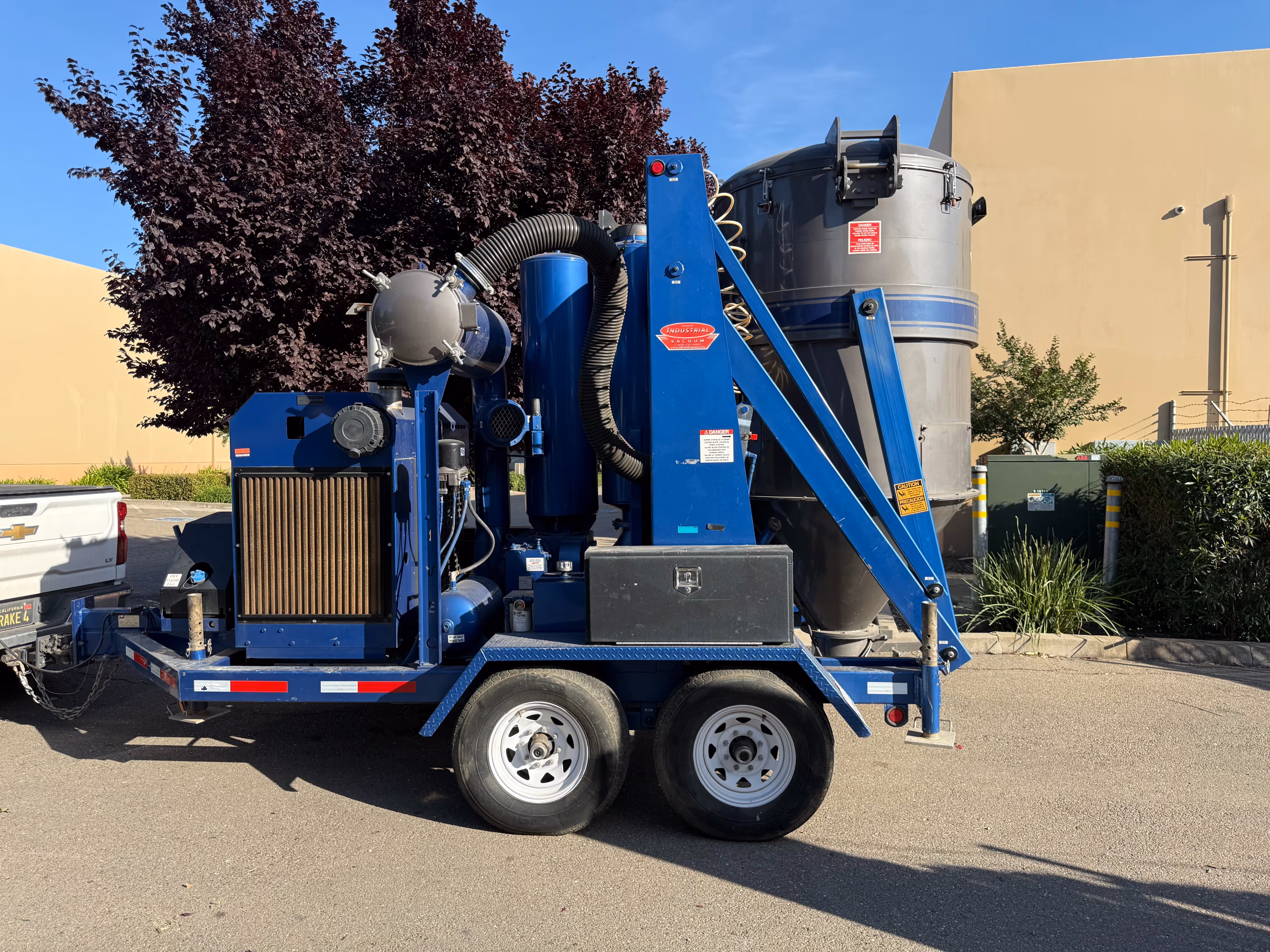 Blue industrial vacuum machine on a trailer parked outdoors beside a white pickup truck.