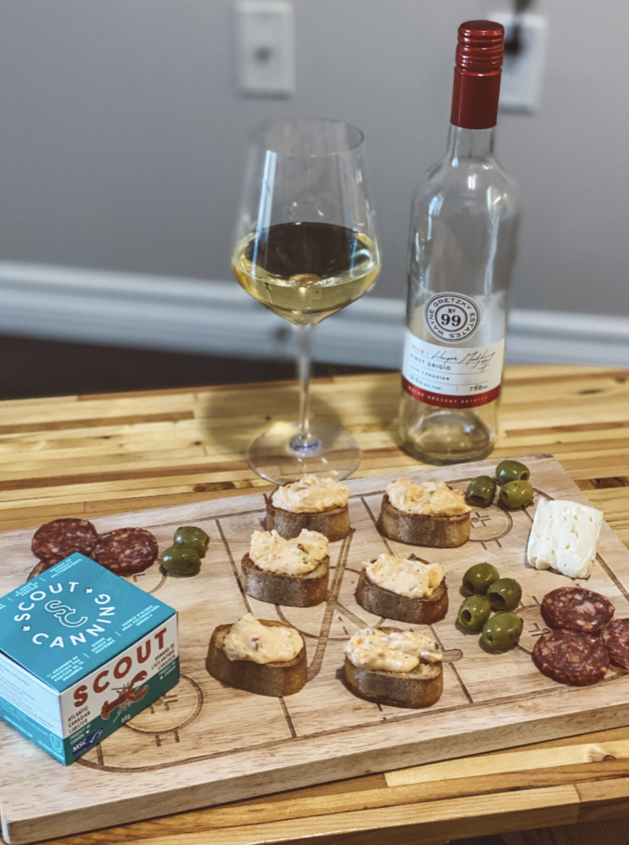 Charcuterie board featuring lobster dip on crackers, paired with salami, cheese, and wine.