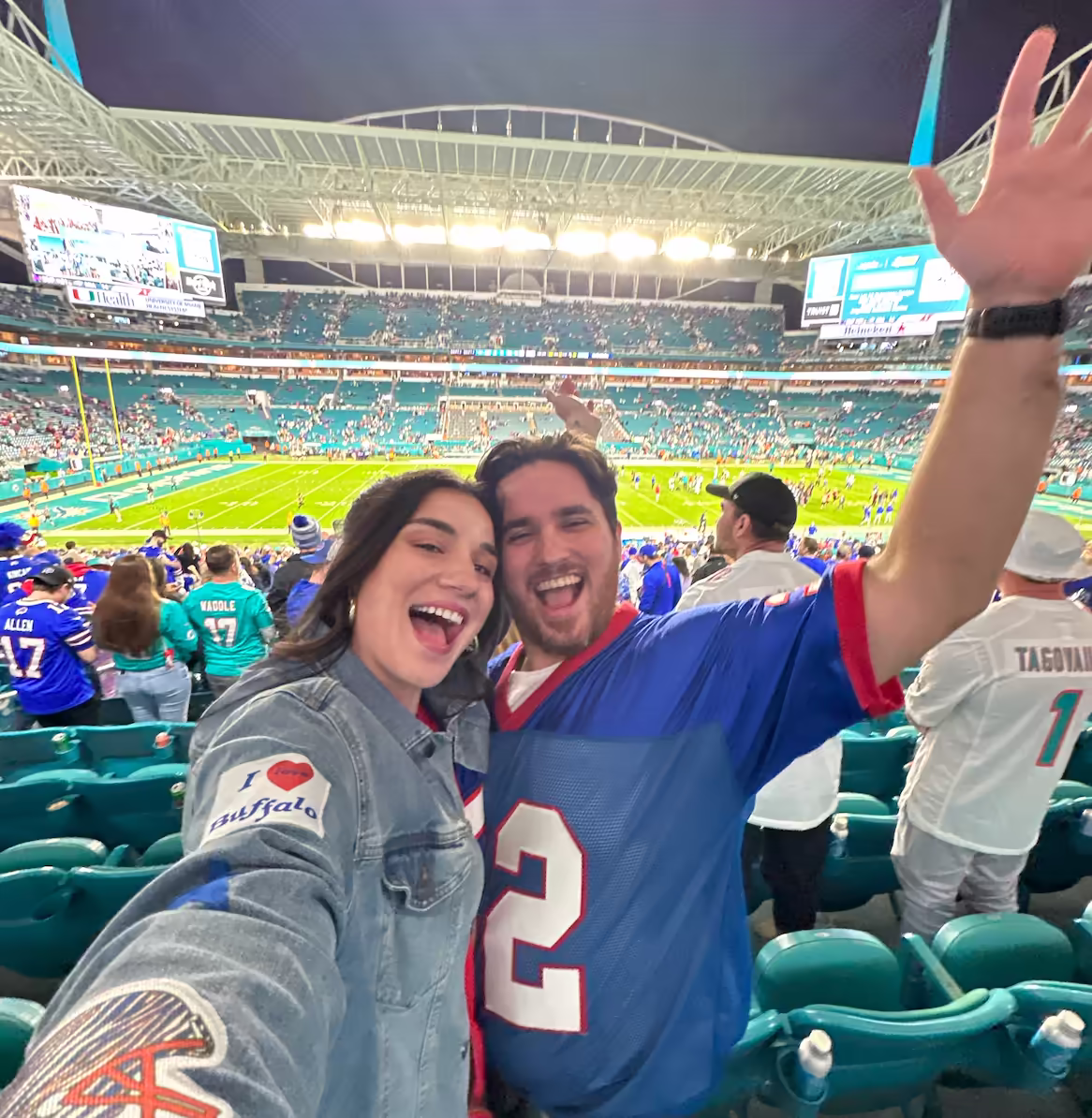Emily and Dean taking a selfie in front of a football stadium during a game.