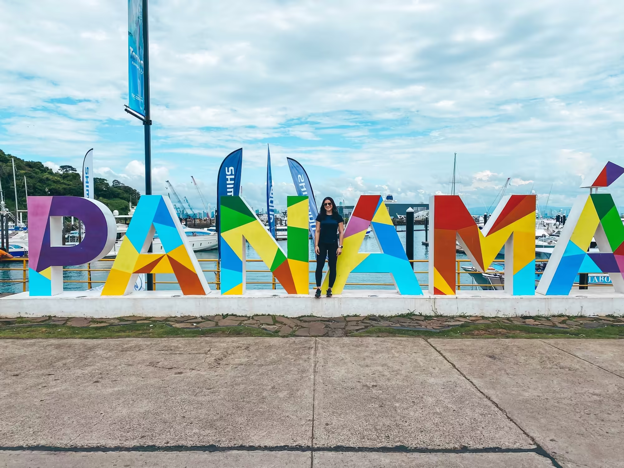 Emily standing in front of the Panama sign in Panama City with the ocean and boats in the background.