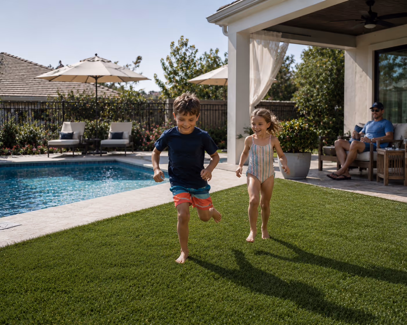 Two children running barefoot on artificial turf by a backyard pool