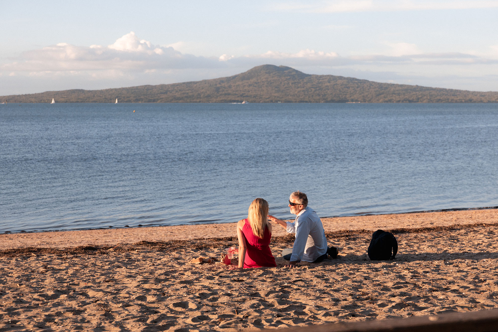 A couple sharing a picnic on St Heliers beach with Rangitoto Island across the water