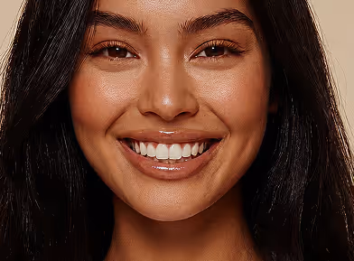 Close-up of a smiling woman with long dark hair and smooth skin against a neutral background.