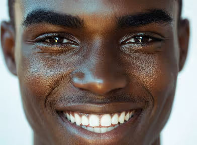 Close-up of a person with dark skin smiling, showing white teeth and expressive eyes.