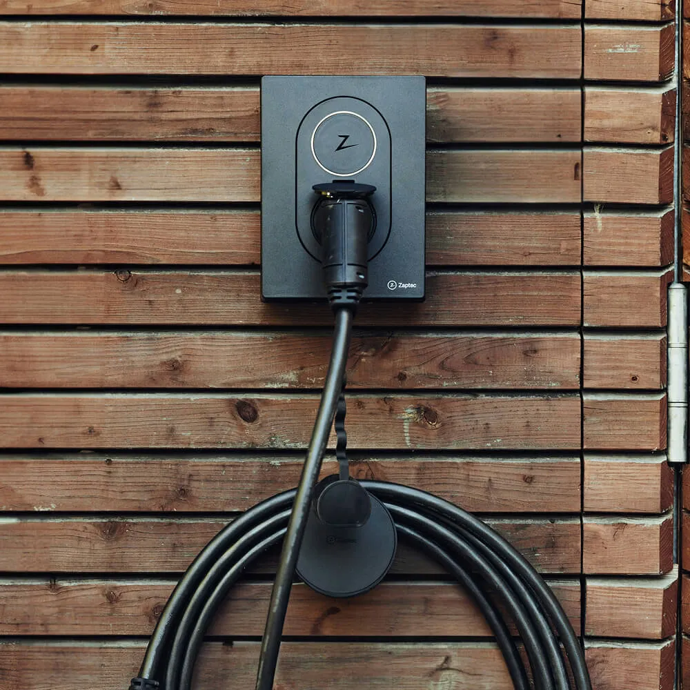 Elektrisk bilopladningsstation monteret på trævæg med sort kabel viklet under den.