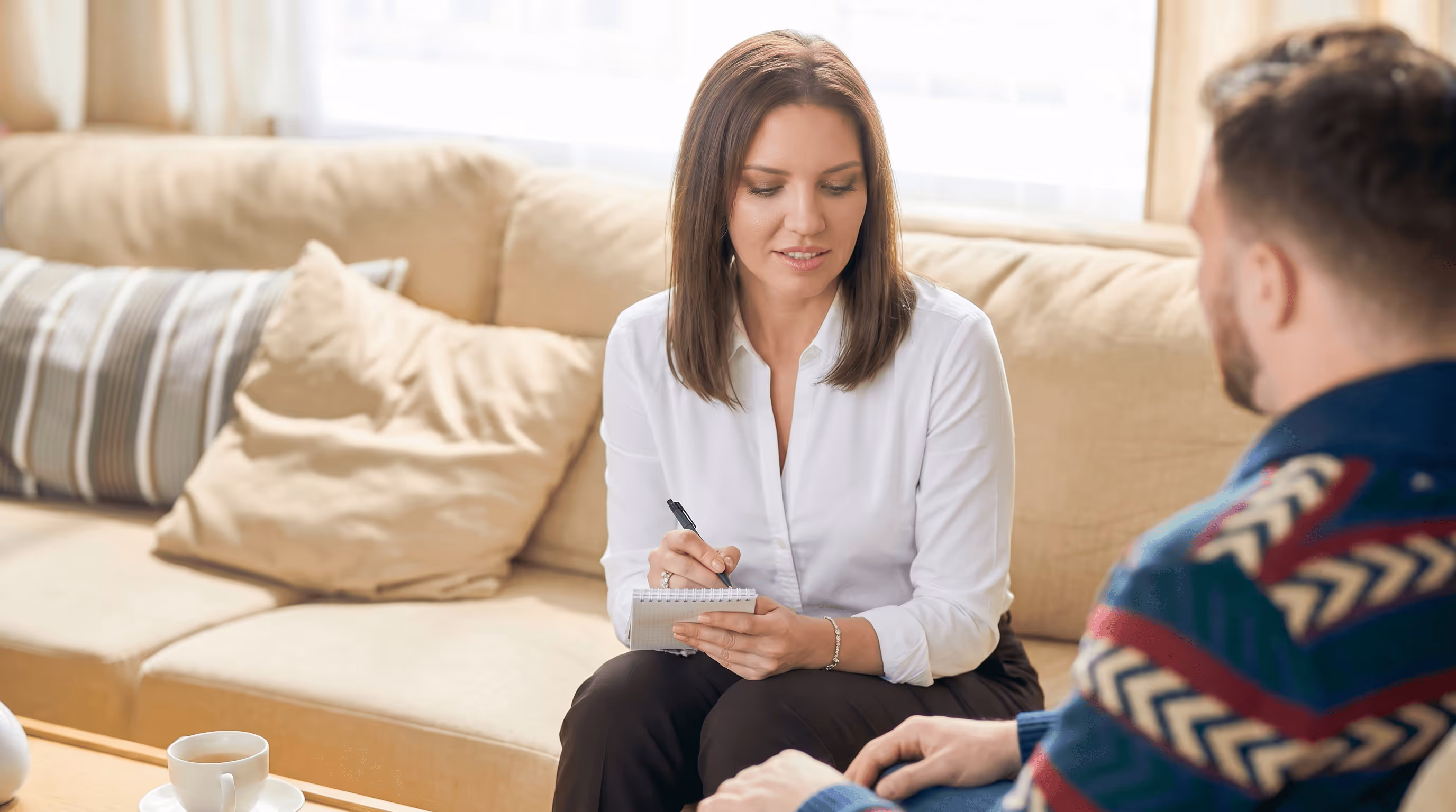 Woman therapist taking notes during counseling session with male client indoors.