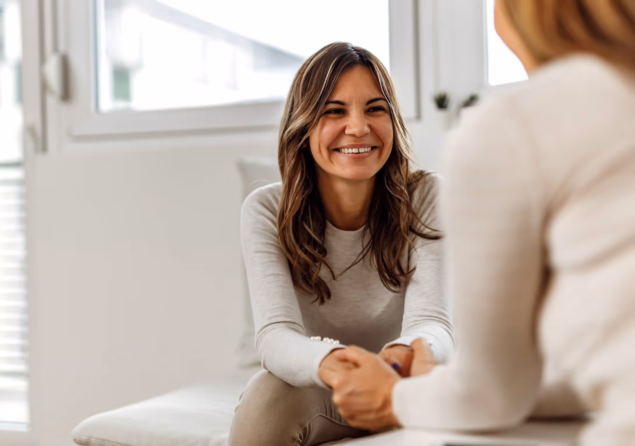 Smiling woman shaking hands with person in bright room with large windows