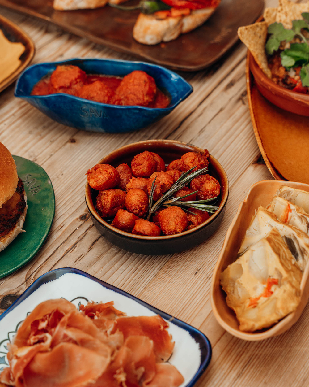 Tapas met chorizo in tomatensaus, serranoham en balletjes op een houten tafel bij Sava