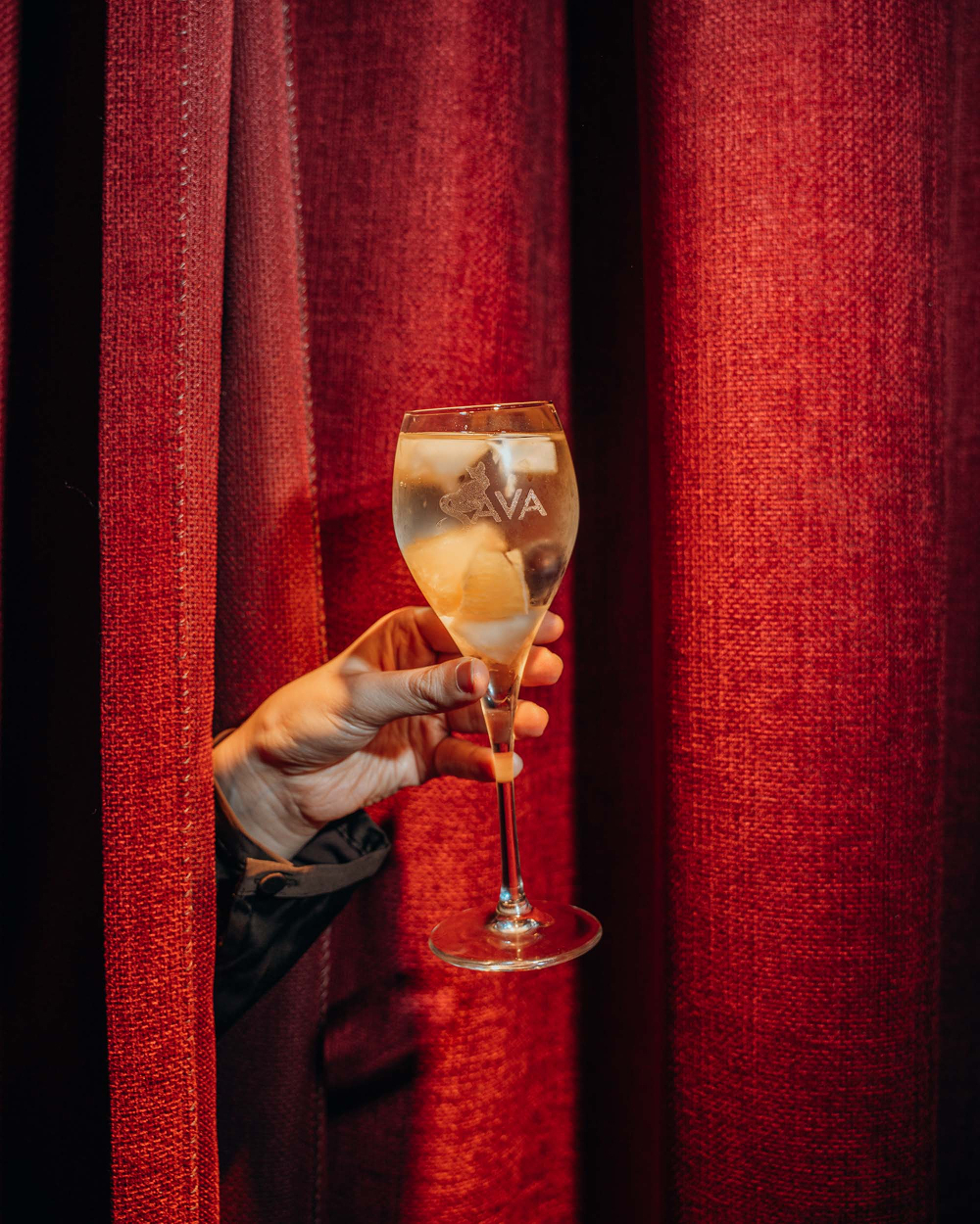 Glas witte sangria met het Sava-logo tegen een rood fluwelen gordijn